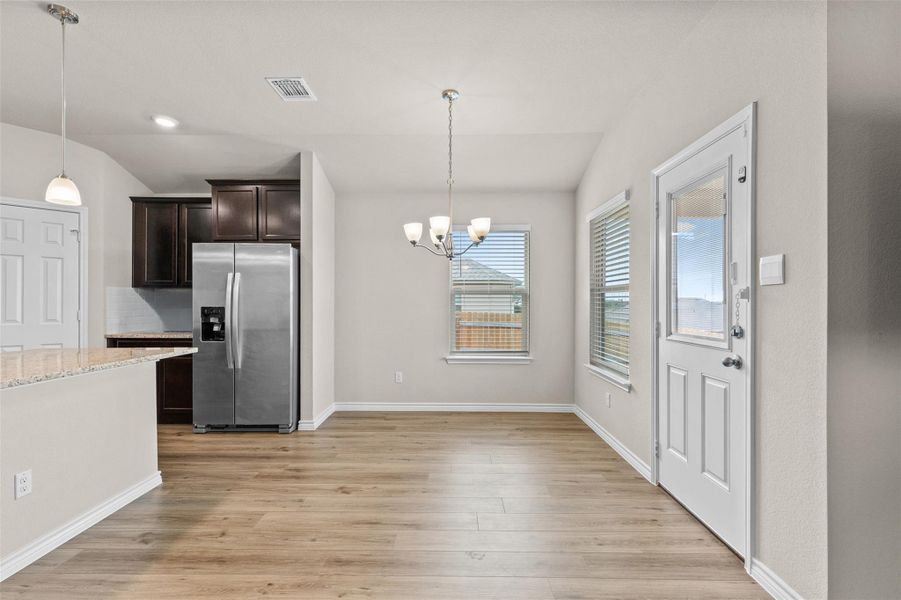 Kitchen with dark brown cabinets, stainless steel fridge, backsplash, light wood-type flooring, and a chandelier