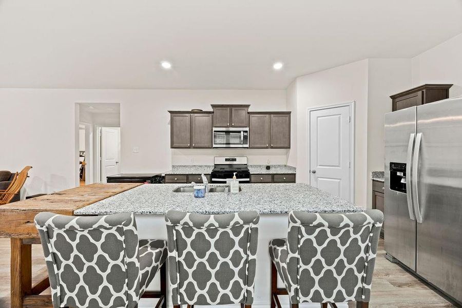 Kitchen featuring a large central island with granite countertop, stainless steel appliances, modern cabinetry, recessed lighting, and wood-finish flooring Kitchen featuring a large central island with granite countertop, stainless steel appliances, modern cabinetry, recessed lighting, and wood-finish flooring