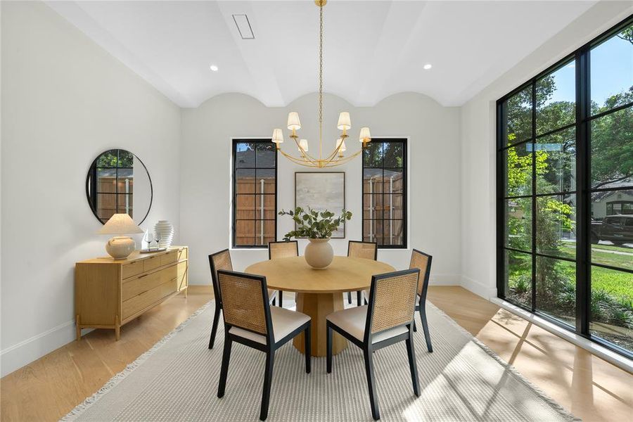 Dining area featuring a gold-finish chandelier, a large picture window, two grid-pattern windows, light wood-finish flooring, and a coved ceiling detail
