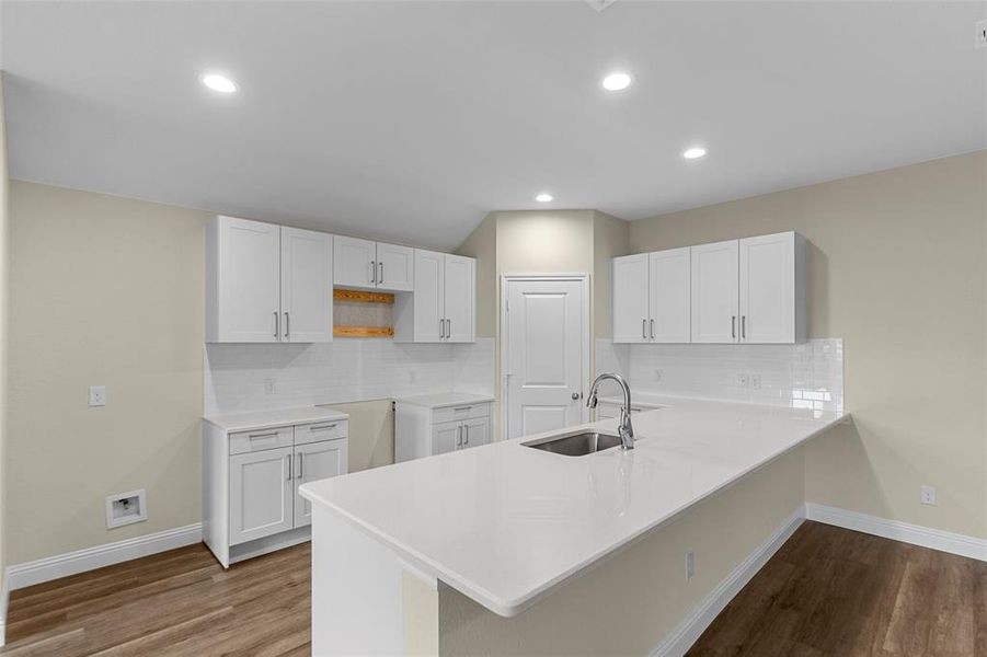 Modern kitchen featuring an island with an undermount sink and gooseneck faucet, white shaker-style cabinetry, white countertops, a subway tile backsplash, and wood-finish flooring