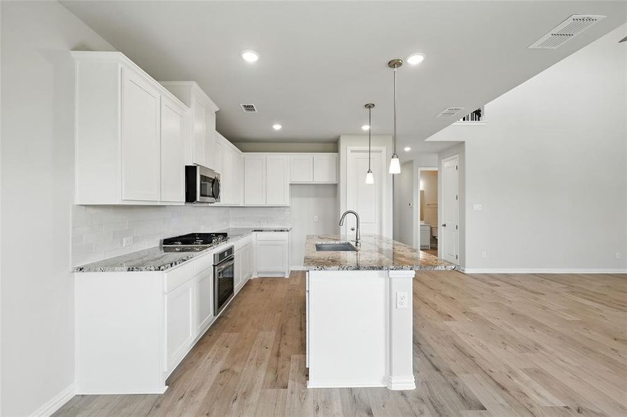 Kitchen featuring backsplash, light stone counters, white cabinets, an island with sink, and recessed lighting Kitchen featuring backsplash, light stone counters, white cabinets, an island with sink, and recessed lighting