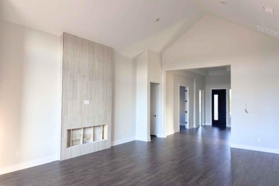 Unfurnished living room with dark wood finished floors, a high ceiling, and a tiled fireplace