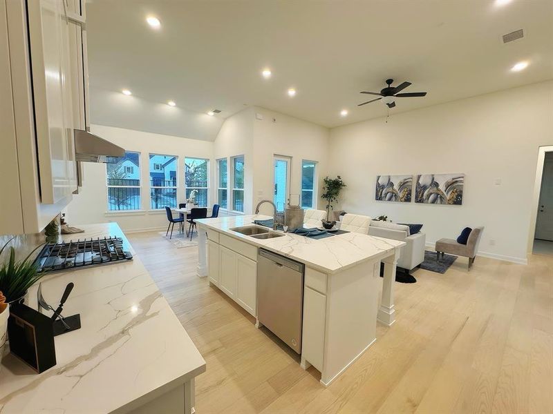 Kitchen with white cabinets, sink, stainless steel dishwasher, an island with sink, and light stone counters