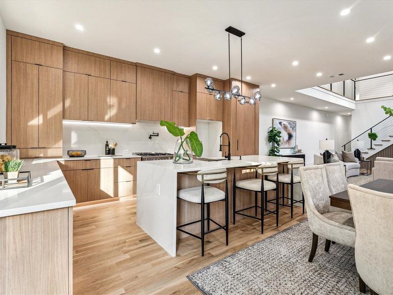 Kitchen with decorative light fixtures, a large island with sink, a breakfast bar area, light hardwood / wood-style floors, and decorative backsplash