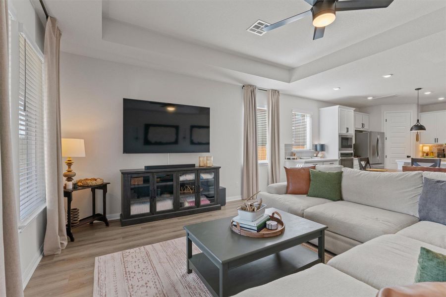 Living room featuring a raised ceiling, light wood-type flooring, a ceiling fan, and recessed lighting
