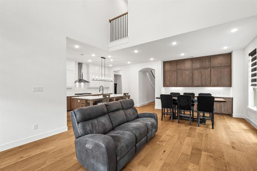 Living area featuring arched walkways, light wood finished floors, ceiling fan, floor plug, recessed lighting, and a high ceiling