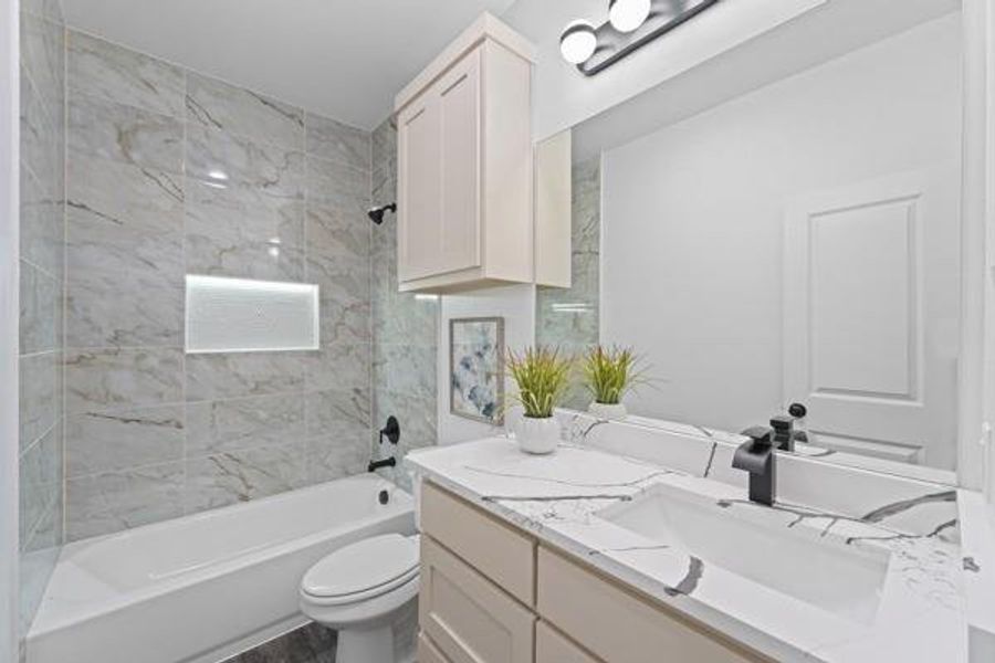 Bathroom featuring a white tub, light-toned marbled wall tiling, and a built-in illuminated shower niche Bathroom featuring a white tub, light-toned marbled wall tiling, and a built-in illuminated shower niche