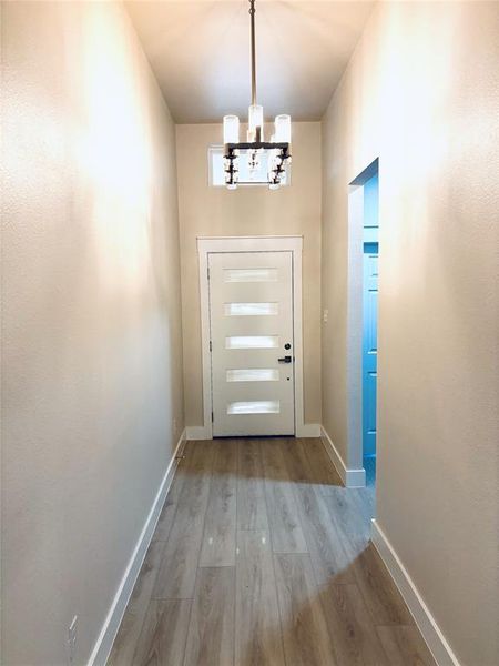 Doorway to outside featuring baseboards, an inviting chandelier, and wood finished floors