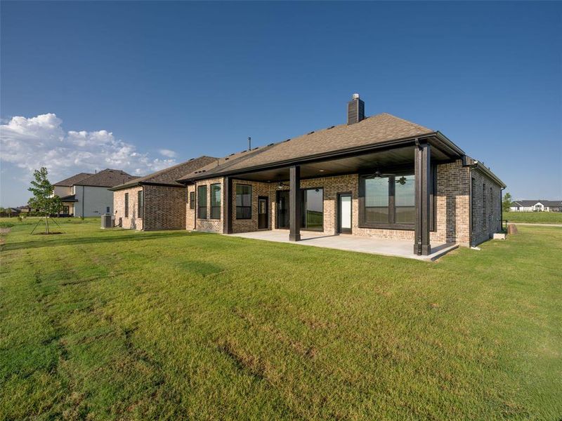 Rear view of property with a patio, brick siding, a lawn, and a chimney