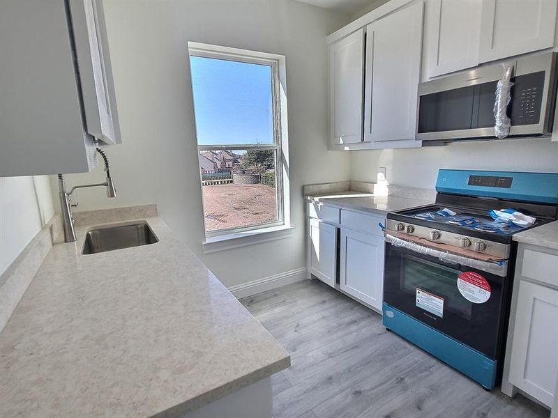 Kitchen featuring light wood-type flooring, stainless steel appliances, white cabinets, and sink