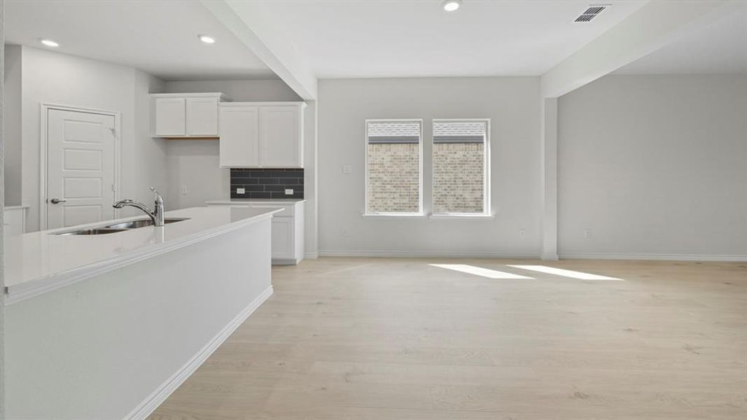 Kitchen featuring white cabinets, backsplash, light stone counters, light wood-type flooring, and recessed lighting Kitchen featuring white cabinets, backsplash, light stone counters, light wood-type flooring, and recessed lighting