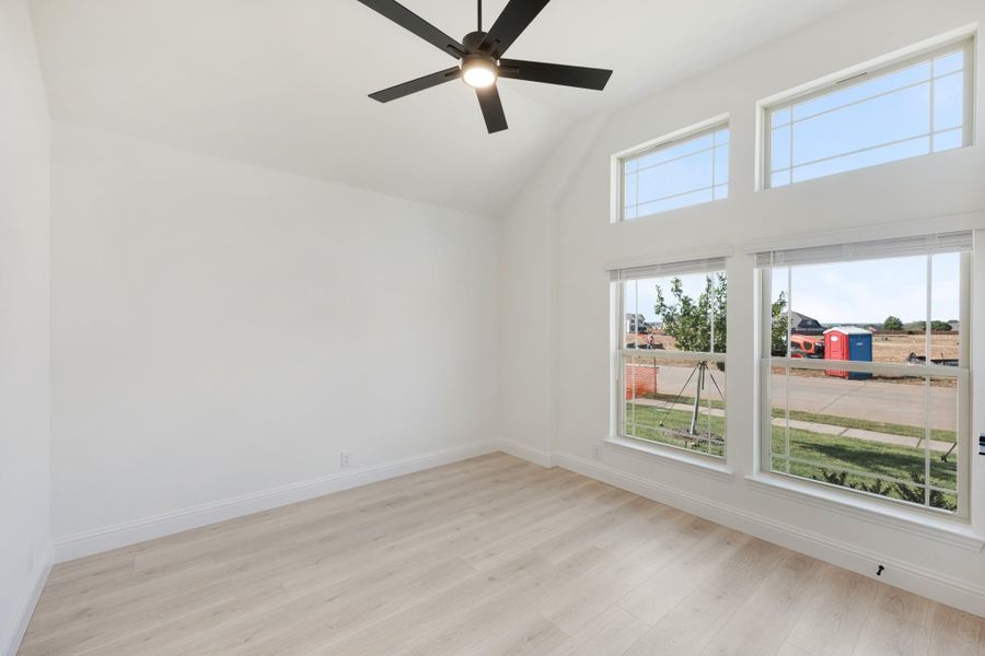 Empty room with vaulted ceiling, ceiling fan, light wood floors, and large windows with neighborhood view