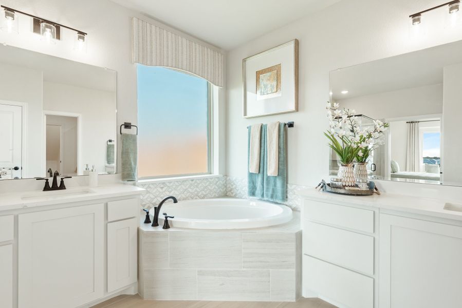 Master bathroom with soaking tub, dual vanities, white cabinets, and large window