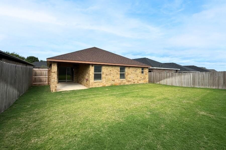 Back of house featuring a patio area, stone siding, a fenced backyard, and a shingled roof