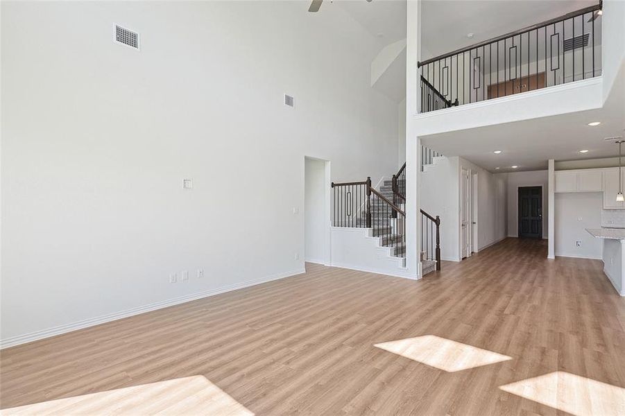 Unfurnished living room featuring ceiling fan, a high ceiling, and light wood-type flooring