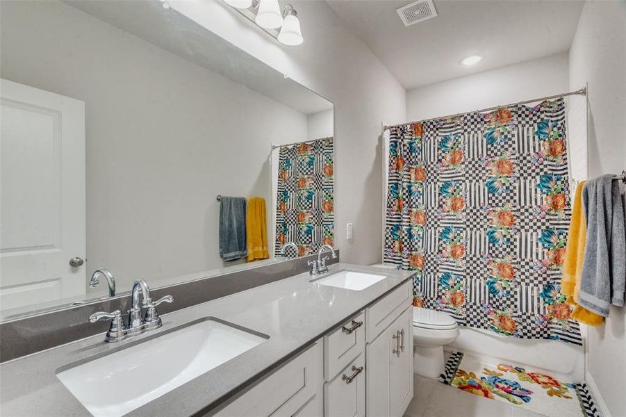 Bathroom featuring tile floors, dual sinks, toilet, and vanity with extensive cabinet space