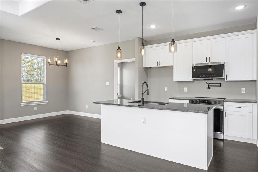 Kitchen with sink, pendant lighting, electric stove, a kitchen island with sink, and white cabinets