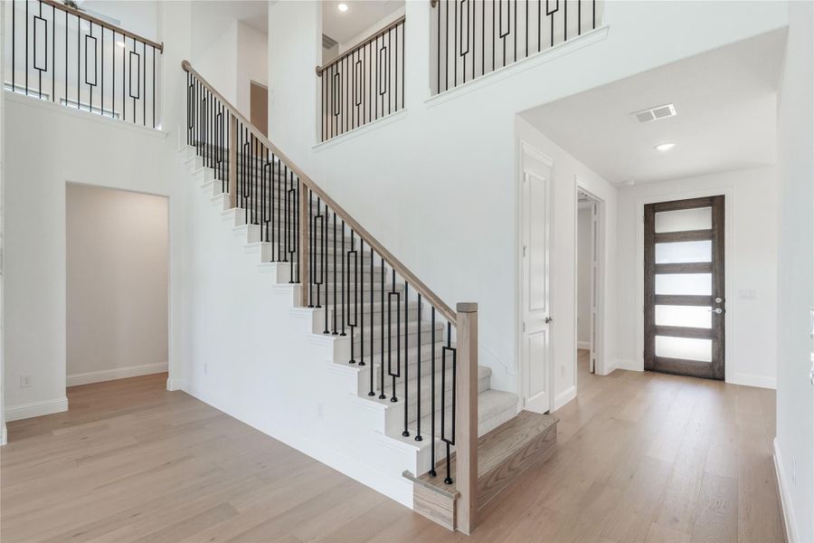 Two-story entryway with staircase featuring black iron balusters, wood handrail, and light hardwood floors near front door