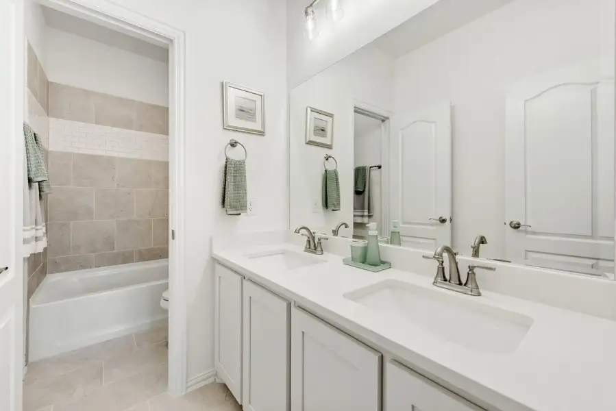 Bathroom with double sink vanity, white countertops, and tiled tub-shower combo in background