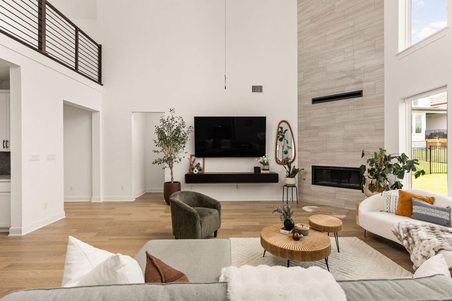 Two-story living area featuring a floor-to-ceiling tile fireplace surround with an integrated linear firebox, high ceilings, wood-finish flooring, and a second-story balcony with metal railing
