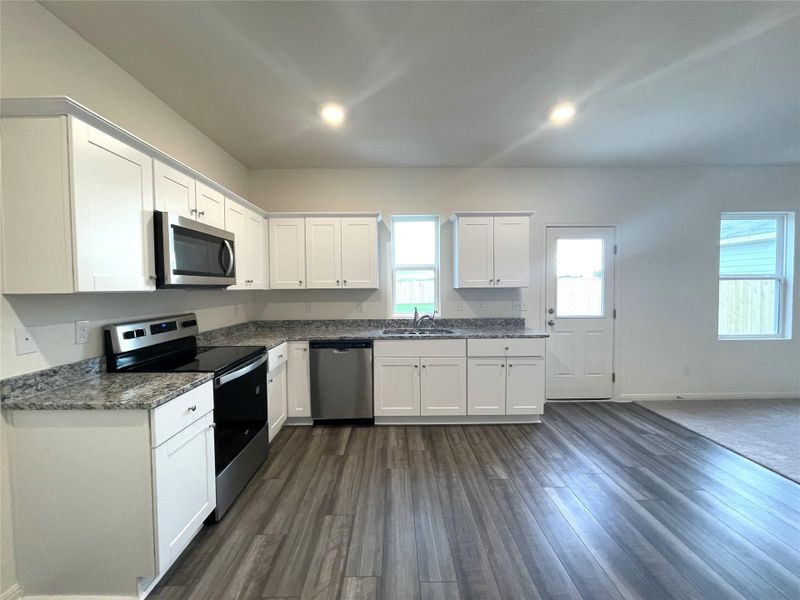 Kitchen featuring dark wood-style floors, baseboards, a sink, white cabinets, and appliances with stainless steel finishes