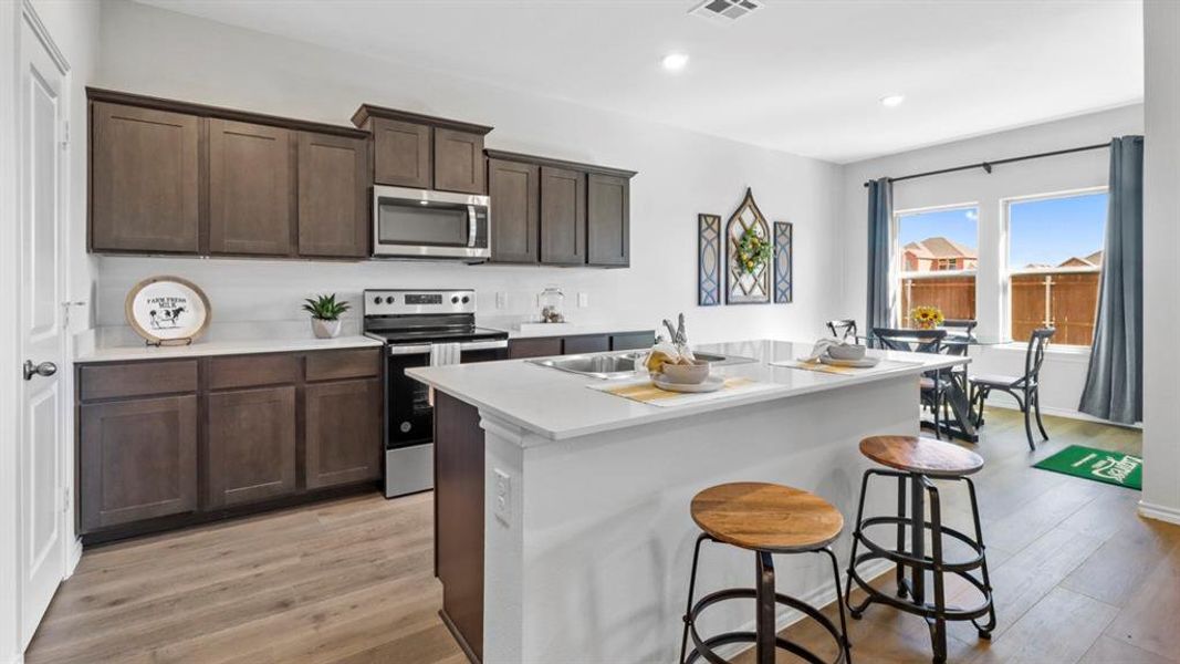 Kitchen with dark wood finish cabinets, stainless steel appliances, a center island with sink, a breakfast bar area, and light wood-style flooring