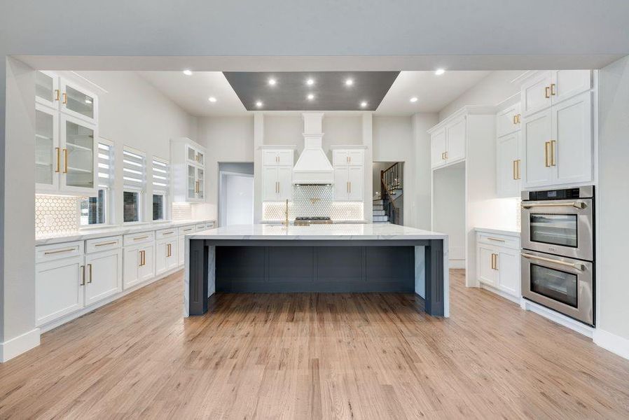 Kitchen featuring a large island, light wood-type flooring, premium range hood, stainless steel double oven, and white cabinetry