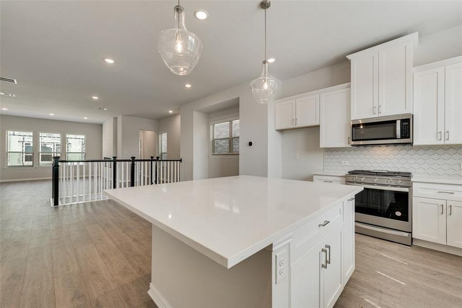 Kitchen featuring light wood-type flooring, white cabinets, a center island, backsplash, and appliances with stainless steel finishes