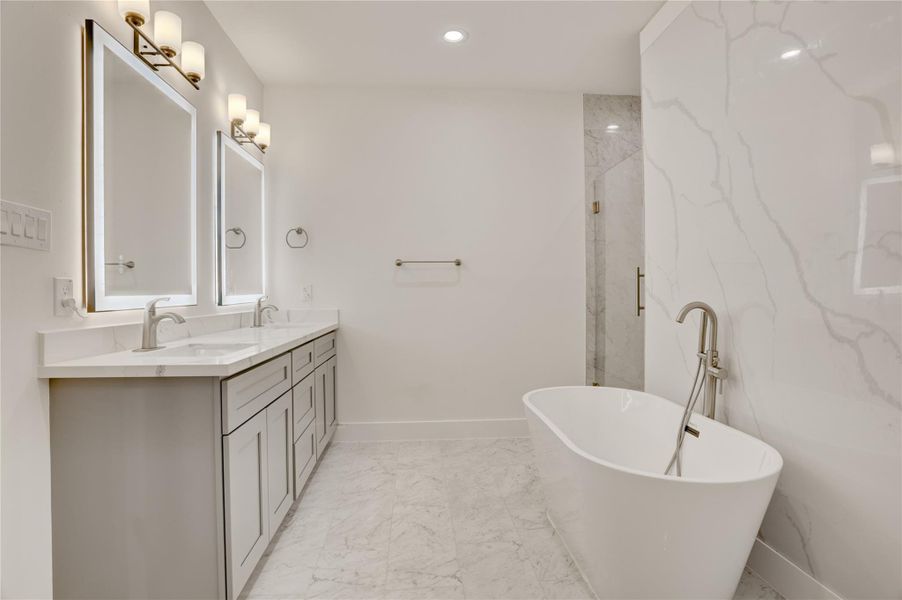 Spa-style primary bath with dual backlit vanities, freestanding tub, and marble-look finishes.