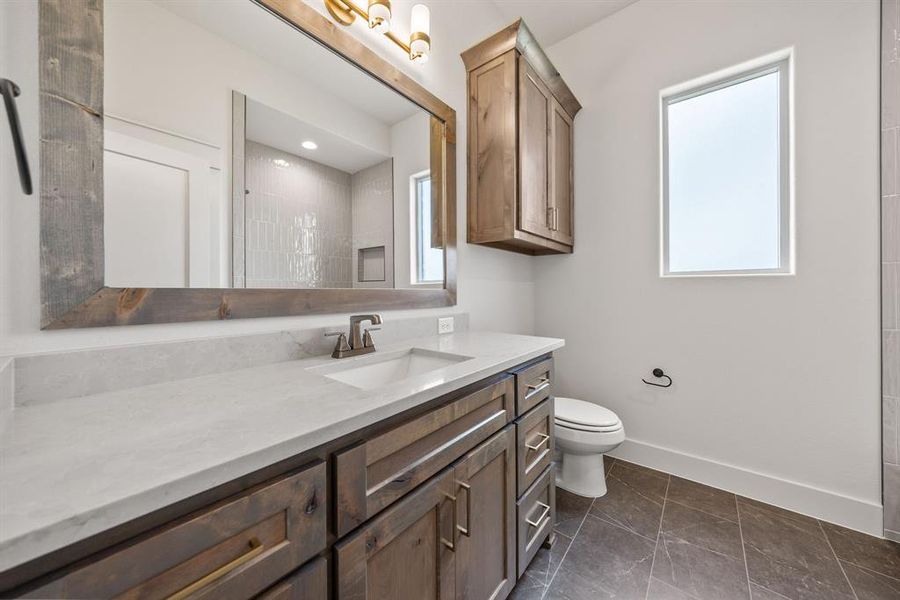 Bathroom featuring a wide wood-framed mirror, wood-finish vanity with ample storage, integrated single sink, and light-toned countertop