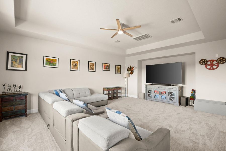 Living room featuring a tray ceiling, light colored carpet, and a ceiling fan Living room featuring a tray ceiling, light colored carpet, and a ceiling fan