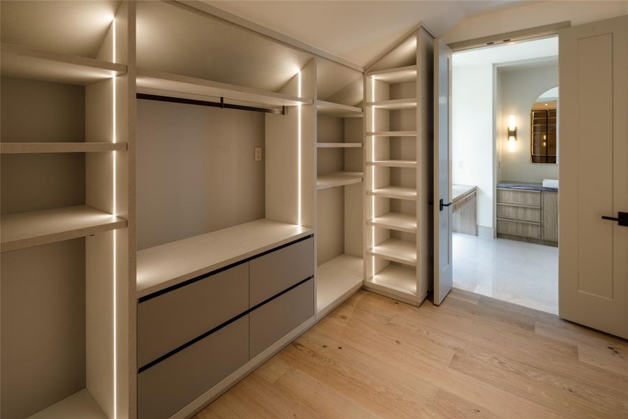 Storage, but make it architectural. Illuminated shelving follows the roofline, while streamlined drawers and custom hanging space use every inch of this oversized primary closet.