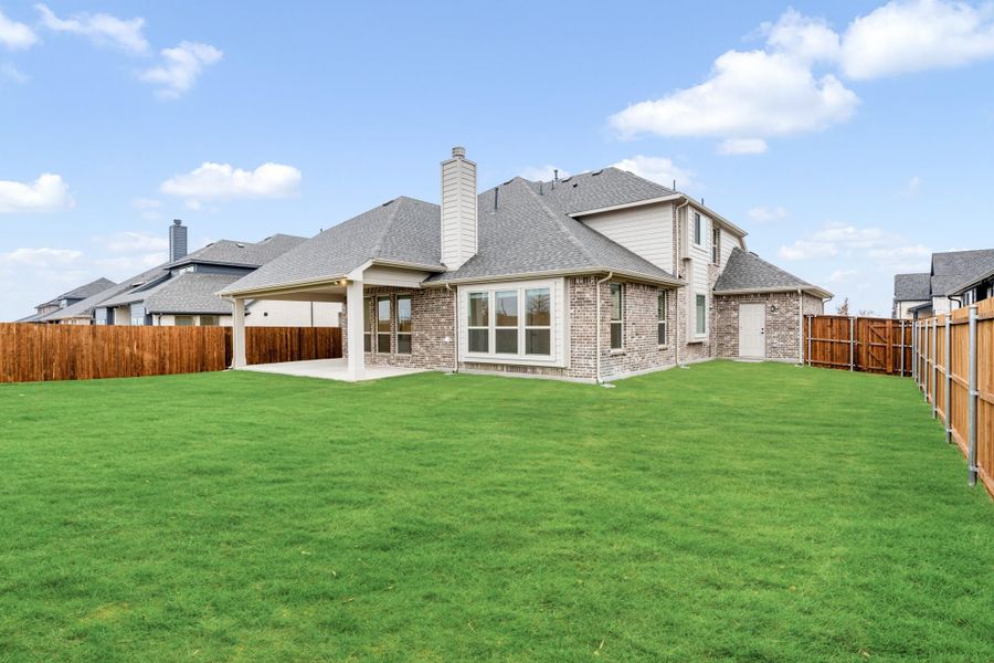 Two-story brick home with covered patio, large grassy backyard, and wood privacy fence Two-story brick home with covered patio, large grassy backyard, and wood privacy fence