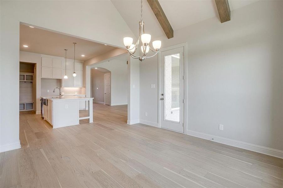 Kitchen with decorative light fixtures, light wood-type flooring, beam ceiling, a chandelier, and a center island with sink