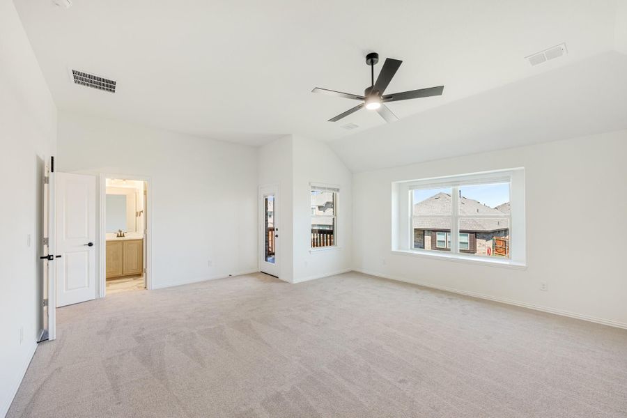 Spacious empty bedroom with vaulted ceiling, ceiling fan, carpet flooring, and ensuite bathroom doorway Spacious empty bedroom with vaulted ceiling, ceiling fan, carpet flooring, and ensuite bathroom doorway