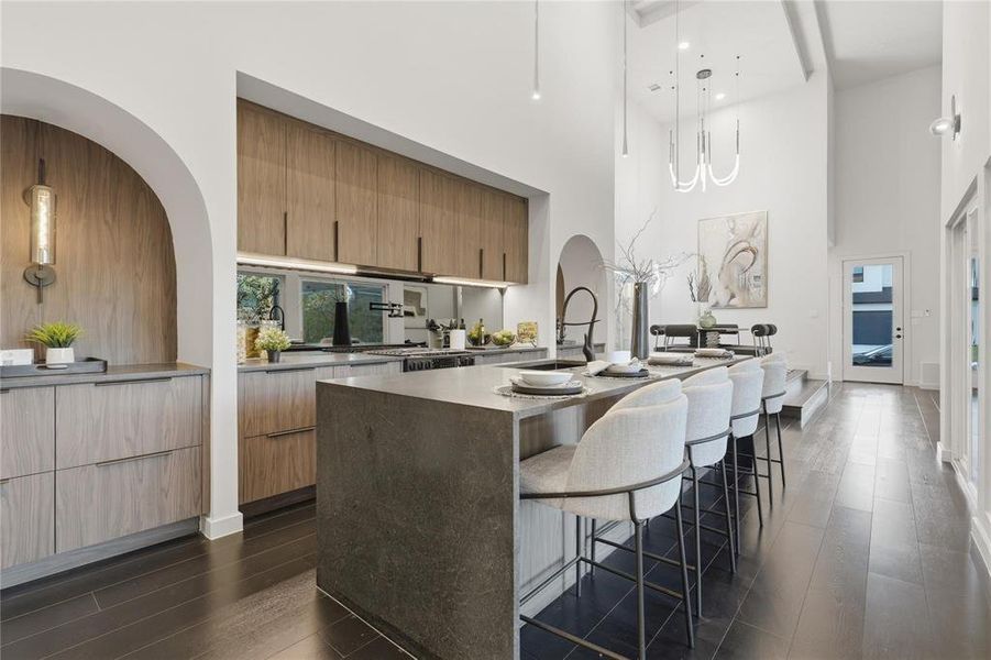 Modern kitchen featuring a waterfall island with integrated seating, dark wood-finish flooring, and high vaulted ceilings