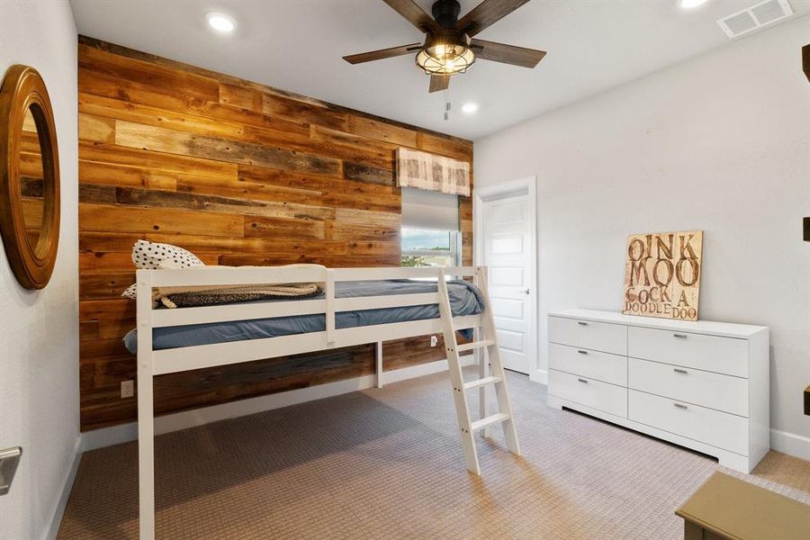 This room features a wood accent wall, a ceiling fan, and carpet flooring throughout.