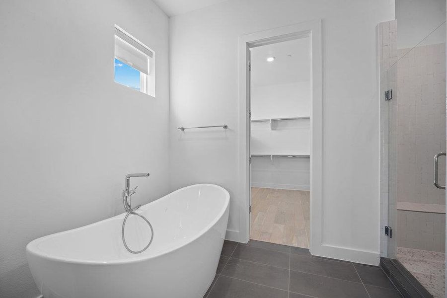 Full bath featuring a walk in closet, dark tile patterned floors, a freestanding bath, and a shower stall