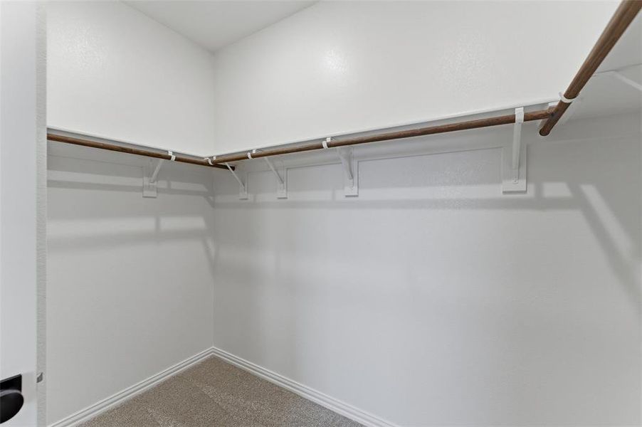 Walk-in closet featuring light-colored carpeting, white baseboards, and a wrap-around hanging rod system
