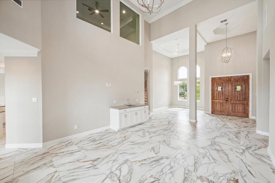 This is a spacious entryway featuring high ceilings, elegant marble flooring, and a statement wooden front door with sidelights, providing a grand and welcoming entrance to the home.