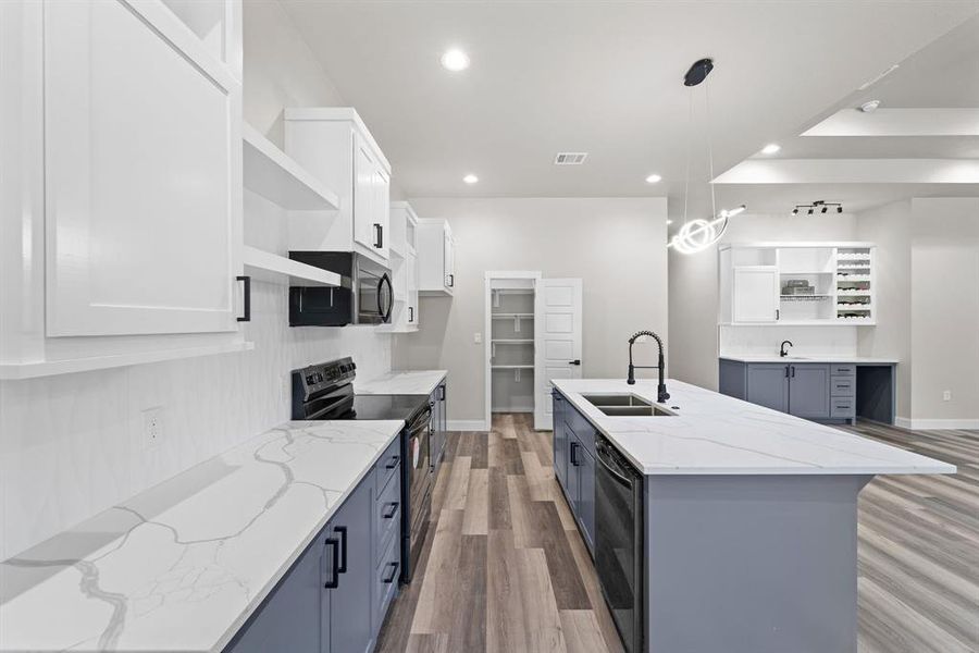 Kitchen featuring an island with sink, sink, hanging light fixtures, white cabinetry, and appliances with stainless steel finishes