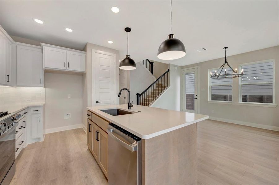 Dual tone kitchen with two tone cabinets, dishwasher, range with gas cooktop, light wood-style flooring, and a kitchen island with sink