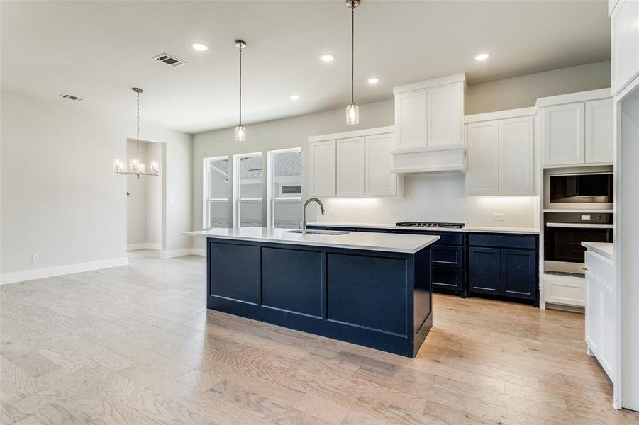 Kitchen featuring sink, hanging light fixtures, light wood-type flooring, decorative backsplash, and stainless steel appliances