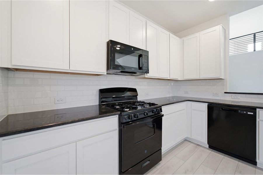 Kitchen featuring white shaker-style cabinetry, dark countertops, black appliances, white subway tile backsplash, and light wood-finish flooring