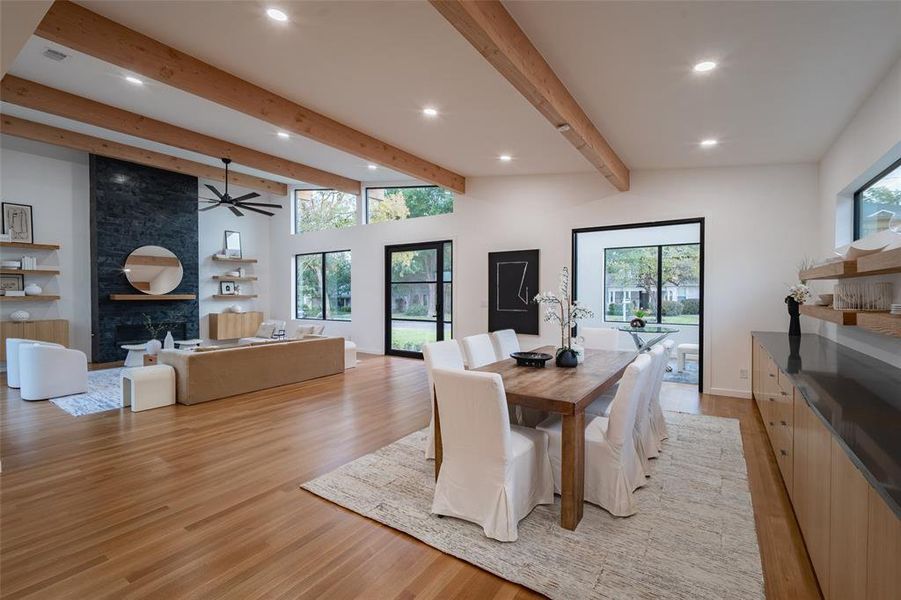 Dining area with ceiling fan, light wood-type flooring, vaulted ceiling with beams, and a large fireplace