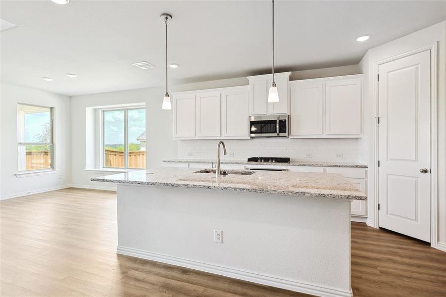 Kitchen with hardwood / wood-style flooring, sink, white cabinetry, decorative backsplash, and a center island with sink