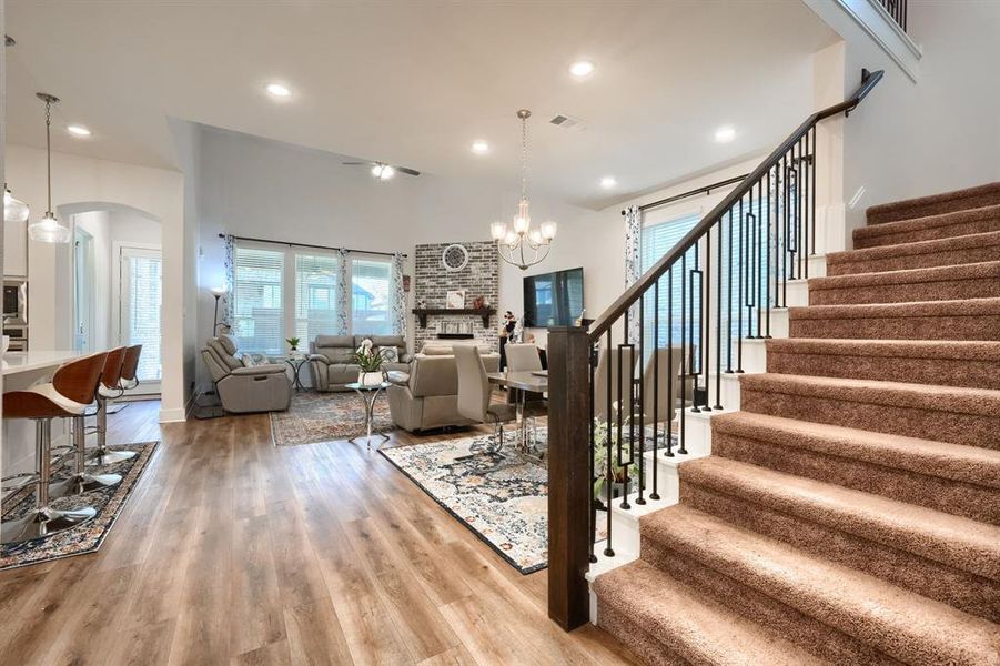 Stairs with wood-type flooring, an inviting chandelier, and a brick fireplace