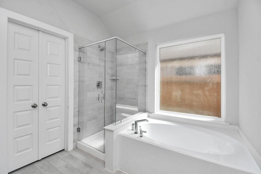 Indulge in a spa-like retreat within the confines of this primary bathroom. Delight in a spacious walk-in shower enveloped in stylish tile surround and unwind in a separate garden tub adorned with custom detailing. Sample photo of completed home with similar floor plan. Actual colors and selections may vary.