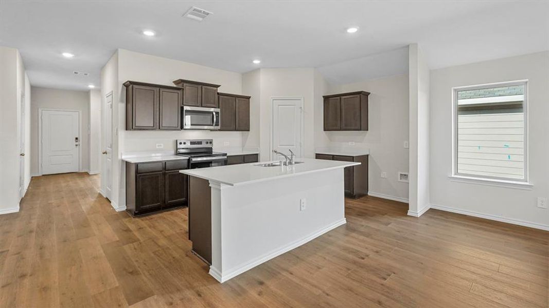 Kitchen with stainless steel appliances, dark wood finish cabinets, a kitchen island with sink, light wood finished floors, and recessed lighting