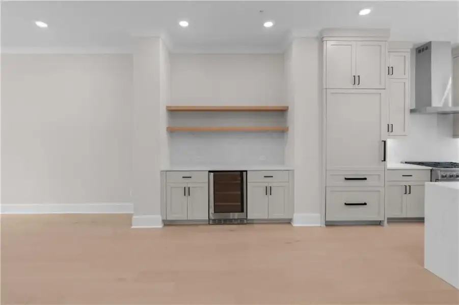 Wood-finish flooring throughout, built-in beverage cooler, light-toned cabinetry, stainless steel range hood, and recessed lighting
